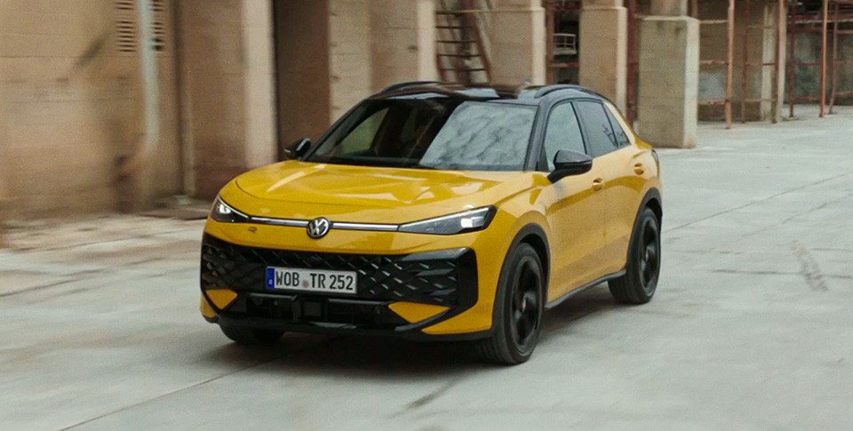 Ein gelber VW t-Roc f&auml;hrt neben einem Haus.